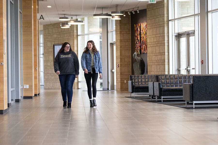 Two students walk together down a hallway, they are looking at each other and laughing.