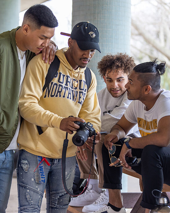Four students gather around a camera and look at the screen