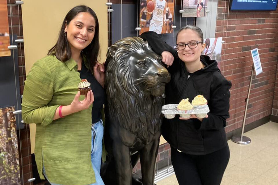 Two students holding cupcakes next to a lion statue