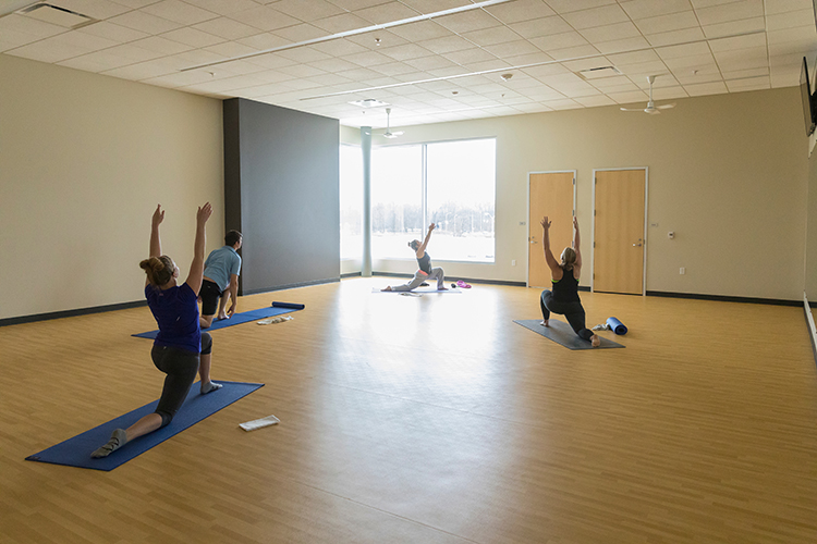 Three people pose on yoga mats facing a teacher who is also on a yoga mat