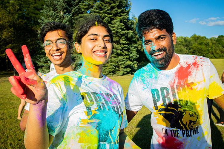 Three students pose together with color powder on their faces and clothes