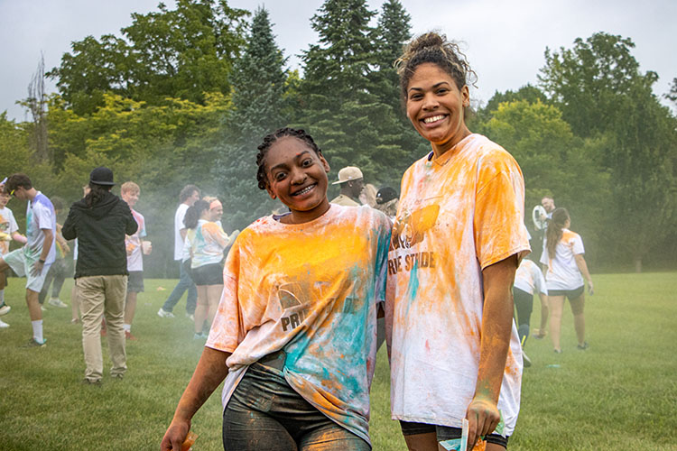 Two students covered in orange and blue color powder pose together