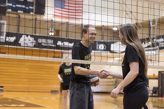 Two PNW students shaking hands underneath the volleyball net in the FRC building.