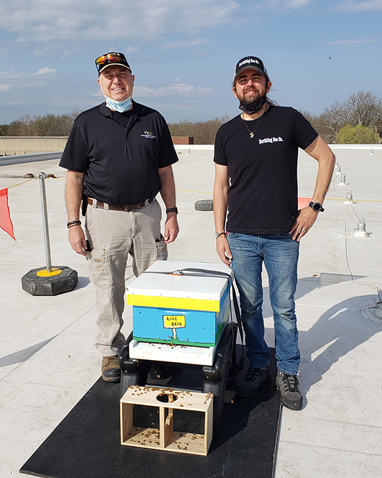 Two men pose with a beehive.