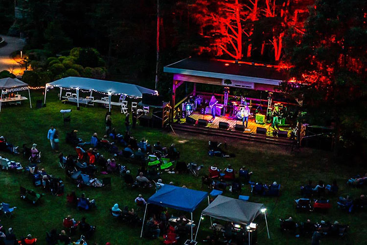 People sitting on a lawn in front of a stage at Gabis Arboretum