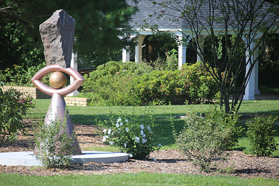 A statue at Gabis Arboretum. There is a gazebo in the background and shrubbery in between.