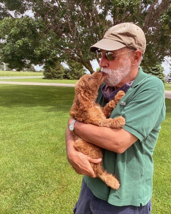 A man in a hat kisses a dog in a yard.