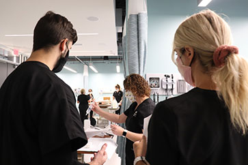 Students in scrubs gather around a student that is holding a syringe