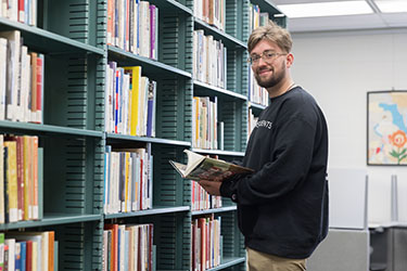 A student reads a book in the library stacks