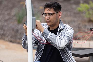 PNW student examining wires on a pole 363x242