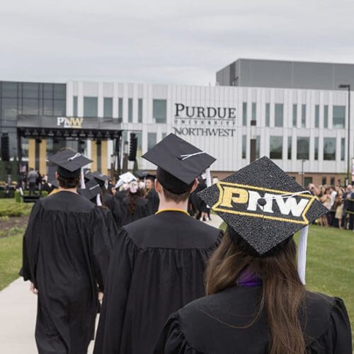 PNW graduates in the procession at spring 2023 commencement. A mortar board decorated with PNW is visible, as is the Nils K. Nelson Bioscience Innovation Building in the background.