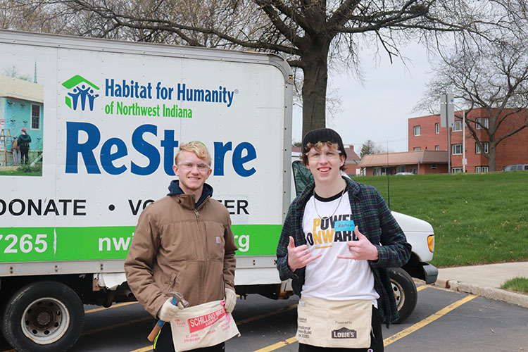 Two students pose together. There is a Habitat for Humanity ReStore truck behind them.