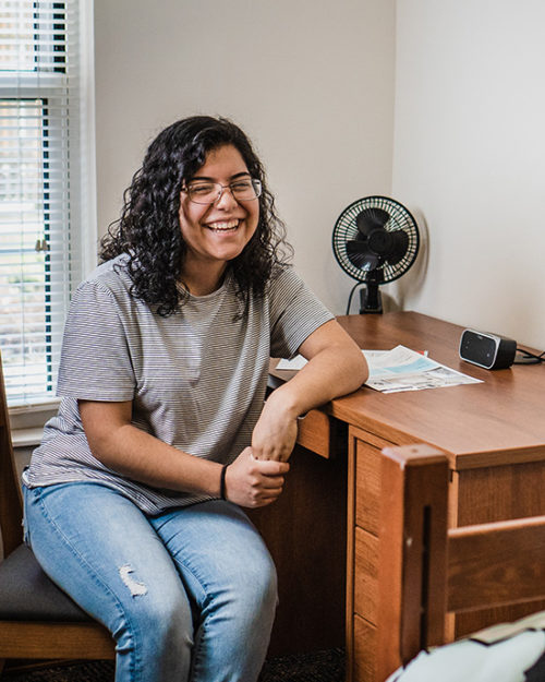 A PNW student laughs in her dorm room.