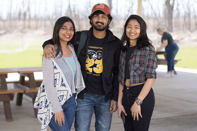 Three students stand together for a photo. The student in the middle has his arm around the student on his left.