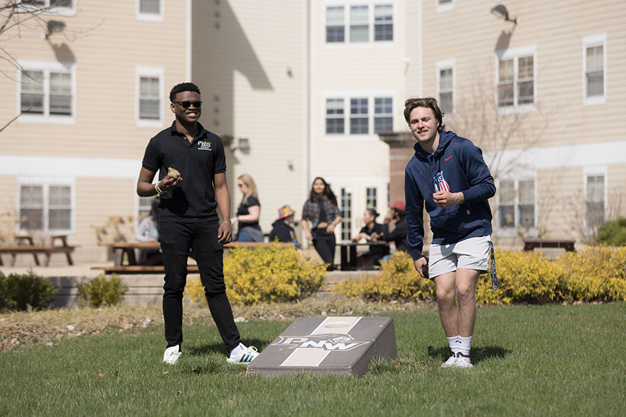 Two students play cornhole outside.