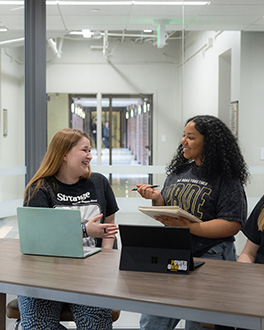 two students talking with laptops in front of them