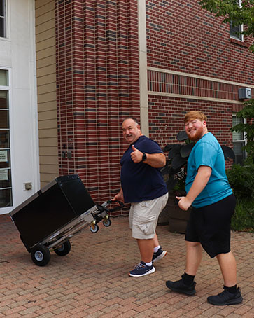 A parent a child move a mini fridge into the dorms
