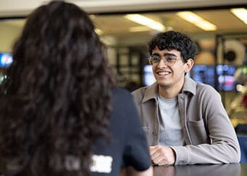 Two students sit at a table outside of Leo's Market in the Classroom Office Building.
