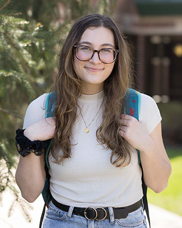 A student stands with their hands on their backpack straps