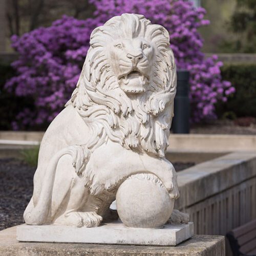 A PNW Lion statue with purple flowers blooming behind it