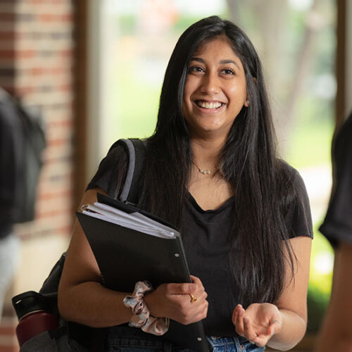 A student smiles while holding a folder.