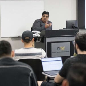 A PNW professor sits at a podium during a class.