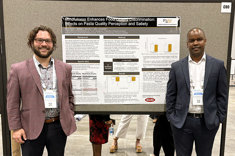 PNW Researchers Matthew Ladwig and Ezra Mutai pose next to a research poster at a scientific conference.