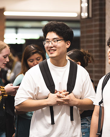 A student in a white t-shirt and backpack walks through a crowd during a campus event.