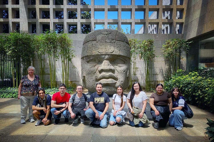 PNW study away students pose in front of an Olmec sculpture