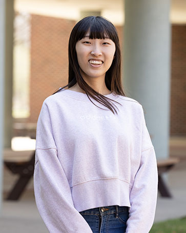 A student stands outside. They are smiling