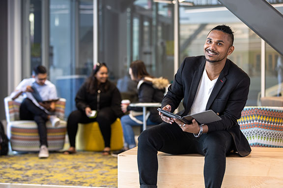 A student in business formal attire sits on a bench and holds an open folder on their lap