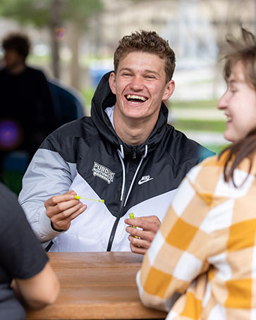 A student sits at a picnic table with other people. They are laughing