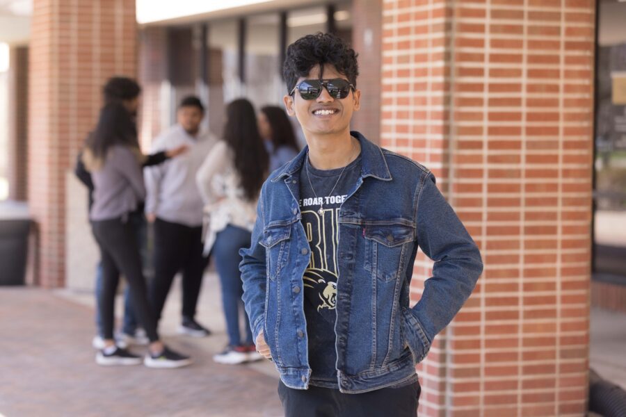 A student wearing sunglasses, a PNW t-shirt and denim jacket poses outside