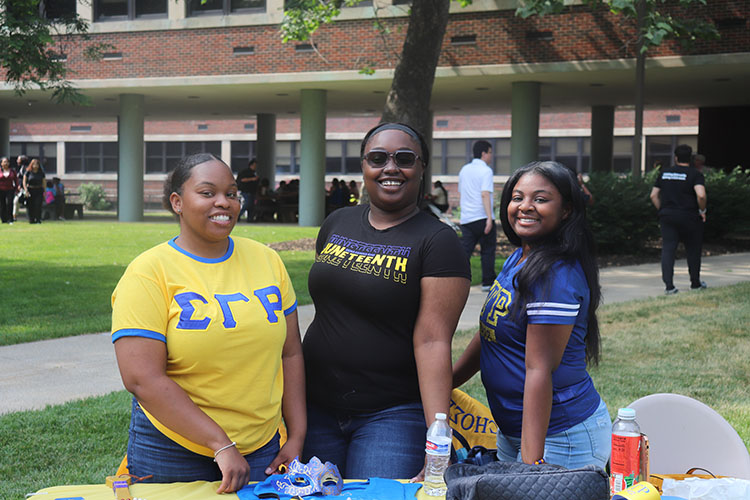 Three students stand behind a blue and yellow table during Juneteenth celebrations