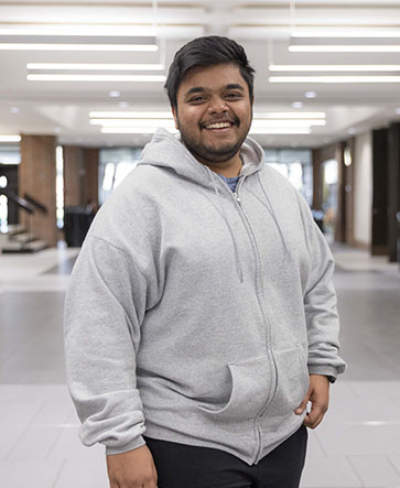 A student in a gray zip up jacket stands in a hallway in SULB