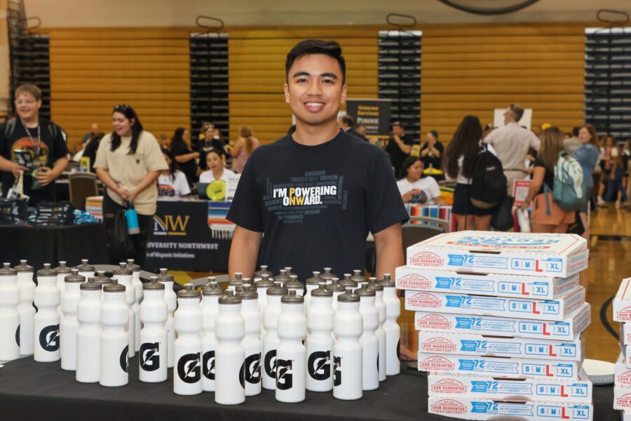 A PNW student stands behind water bottles and pizza at the Westville Welcome Rally