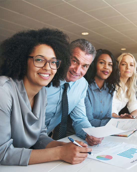 Four people in business attire lean over a table and look toward the camera