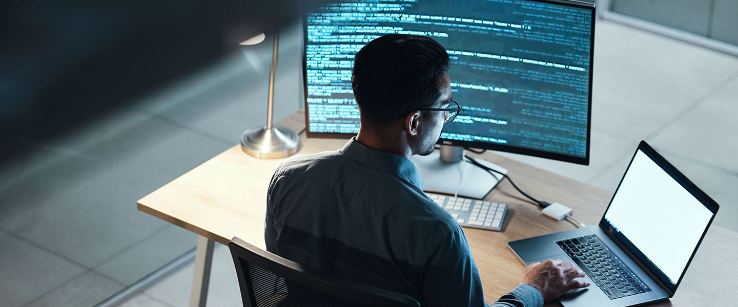 A person sits at a computer and works on a program at night.