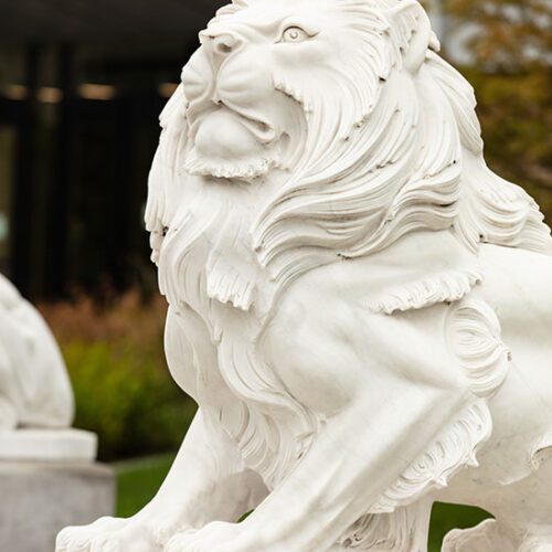 A lion statue with a building and greenery in the background