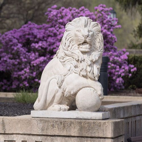 A PNW lion statue on the Westville campus. There are purple flowers blooming behind the statue