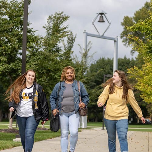 Three students walk together outside. The PNW bell tower is in the background