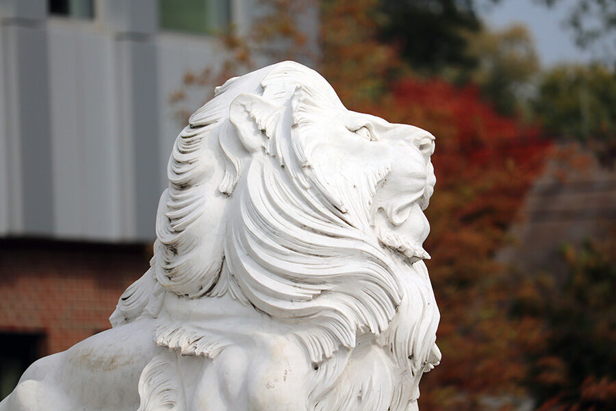 A lion sculpture in front of fall foliage