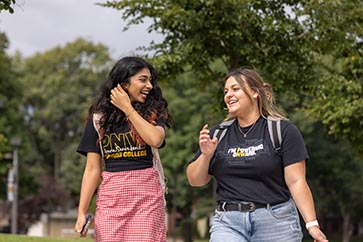 Two PNW students walking and laughing outside on campus in PNW t-shirts 363x242