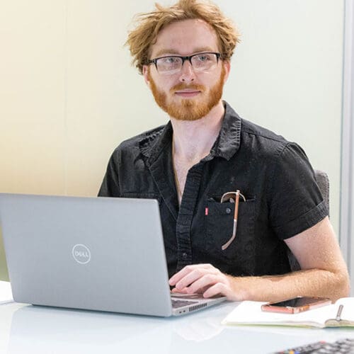 A student sits at a table. There is a computer on the table in front of them.