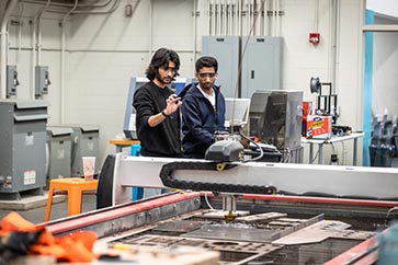 Two PNW students with safety goggles on looking at a piece of equipment 363x242