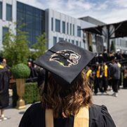 A student poses during commencement. They are facing the stage and have a bedazzled PNW Lion logo on their cap.