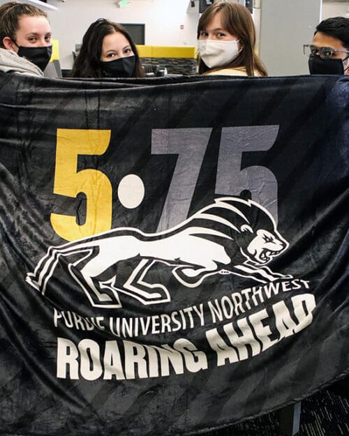 Students holding a blanket that says 5-75 Roaring Ahead