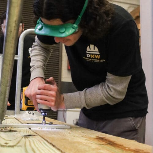 PNW Construction Club president Clayton Whiting drills bolts into the picnic table’s legs to secure them.