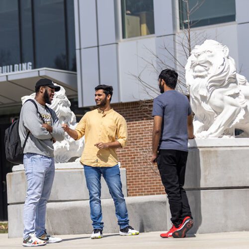 Three students stand outside, near lion statues