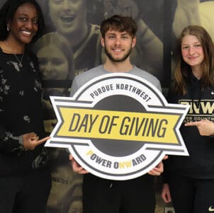 Three students pose with a "Day of Giving" sign